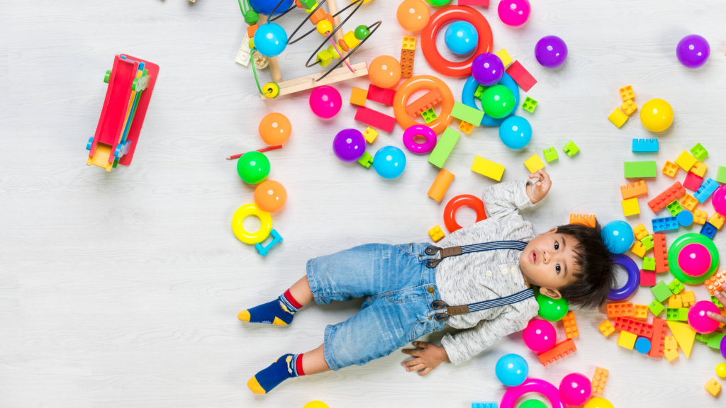 young toddler laying down in a mess of toys, something a toy rotation solves